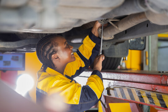 Small business garage, mechanic, African female engineer handling car exhaust repair confidently, technical performance shines in automotive uniform with strong leadership engineering task in workshop - Powered by Adobe