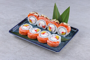 Salmon-wrapped sushi rolls filled with shrimp, mango, cream cheese, and roe, topped with almond slices and served on a decorative plate