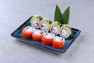 Colorful sushi rolls with salmon, avocado, shrimp, cream cheese, and roe, topped with sauce and crunchy bits, served on a blue rectangular plate.
