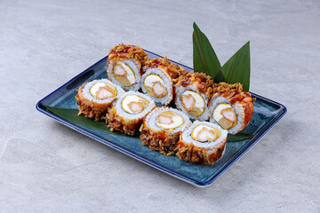 Crispy sushi rolls filled with shrimp, cream cheese, and egg, topped with fried onions and sweet sauce, served on a blue ceramic plate.