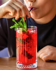 Little kid boy drinking healthy fruits and vegetables juice smoothie. Kid hold the glass with pink cocktail with ice and slice of strawberry