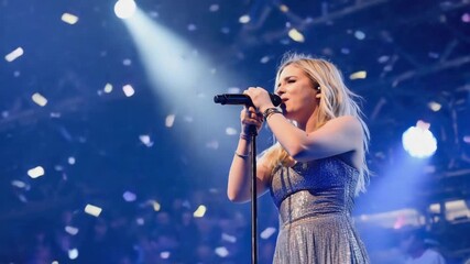 Young female singer captivating an audience while performing live on a vibrant stage, surrounded by dazzling lights and falling confetti, creating an exhilarating concert atmosphere - Powered by Adobe