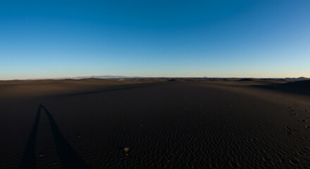 Vast expanse of dark volcanic sand stretches under a clear blue sky.