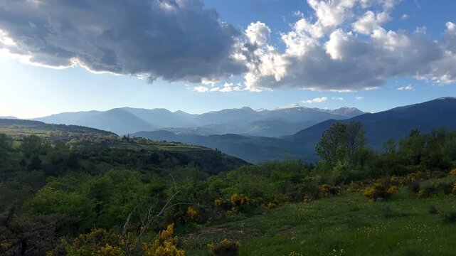 Scenic view of rolling hills, mountains, and a cloudy sky under sunlight. Mountain range with wildflowers. Landscape with Rolling Hills and Cloudy 