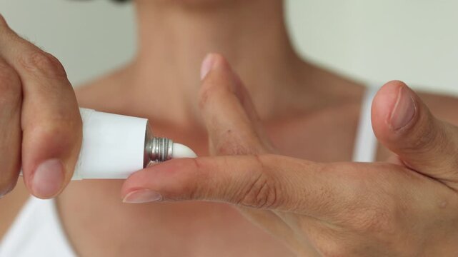 Woman Applying ointment from White Tube on Finger &ndash; Skincare, Treatment, Dermatology, Close-Up of Hands with Soft Focus Face in Background