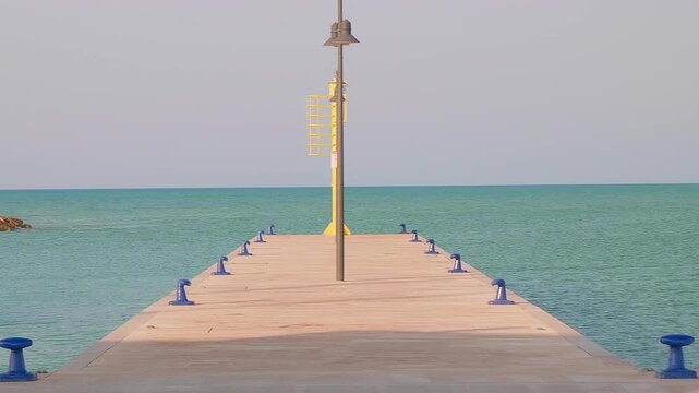 A stone pier leads into tranquil blue sea at Rodi Garganico&rsquo;s port, featuring a green beacon, rocky breakwater, and clear sky&mdash;perfect for maritime themes and coastal serenity.