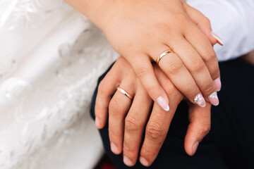 A closeup of a couple's hands with gold wedding rings resting together on a white fabric.