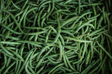 Top view of heap raw green pods at local farmers market in daylight, organic vegetable at grocery store, healthy food and seasonal produce, not cooked asparagus beans, selected focus