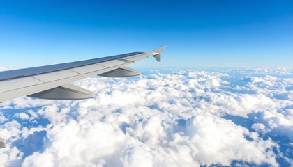 Obraz premium A stunning panoramic view from an airplane of a wing soaring high above a sea of fluffy white cumulus clouds under a clear deep blue sky.