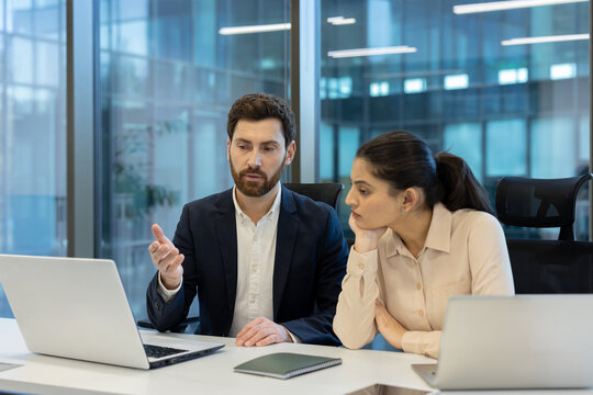 A business team is engaged in a discussion, looking at a laptop in a modern office environment.