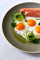 A beautifully arranged plate featuring sunny-side up eggs accompanied by sausages and fresh vegetables, showcasing a delightful breakfast dish perfect for any morning.