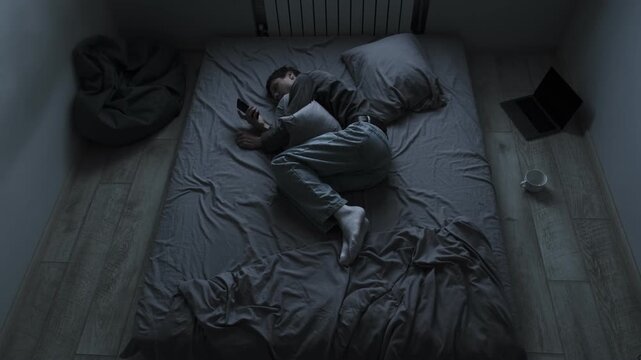 Broken heart after breakup. Young man lying in bed hugging pillow looking at photos of ex girlfriend feeling pain and wanting to text her.