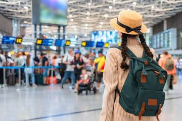 Back view of woman in an elegant suit, straw hat and backpack in airport. Copy space. A blurred...