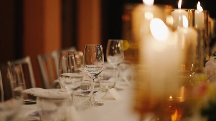 Close-up of elegant candles in glass holders glowing warmly on a decorated dinner table at night. Romantic and cozy atmosphere, perfect for weddings or special events.