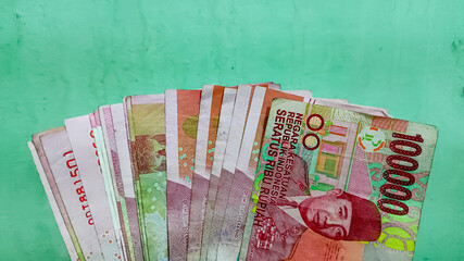 A fanned-out collection of Indonesian Rupiah banknotes against a solid green background.