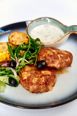 Deliciously prepared meat patties served with fresh salad and a tangy dipping sauce, showcasing vibrant colors and textures on a stylish plate