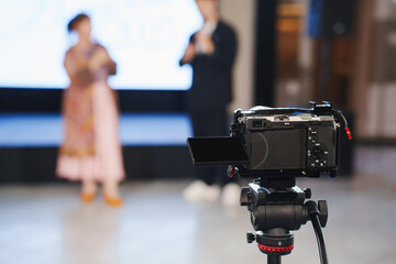 Camera on tripod capturing presentation at indoor event