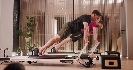 Two individuals engage in a pilates session, demonstrating various exercises for core strength and flexibility. The setting features sleek equipment and a minimalist design - Powered by Adobe