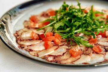 A Deliciously Prepared Plate of Thinly Sliced Octopus Carpaccio Garnished with Fresh Tomatoes and Arugula on a Stylish Plate