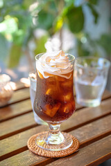 A real photo of an ice americano with whipping cream on wooden table in a relaxing cafe in afternoon