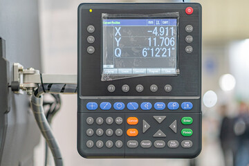 Close-up photograph of a digital multimeter mounted on industrial equipment in a technical workspace, with a blurred background suggesting activity