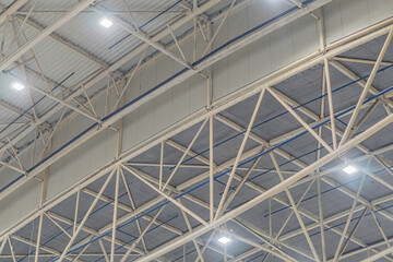 Large industrial hangar or warehouse with high ceilings, metal beams, and trusses Muted color palette consisting of grays and metallic hues Diffused natural light suggests skylights Empty interior