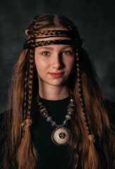 Mystical portrait of young girl with tribal braids and ethnic jewelry in dark background