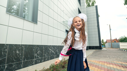 School Girl happy about beginning school year. girl with school bag, running for joy against background of school building. child is happy to start lessons. The concept of education