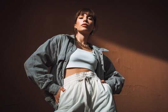 Confident young woman posing stylishly in casual urban outfit with dramatic lighting and strong attitude