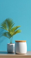 Obraz premium Two white ceramic pots, one with a lid, hold a small palm plant against a teal wall
