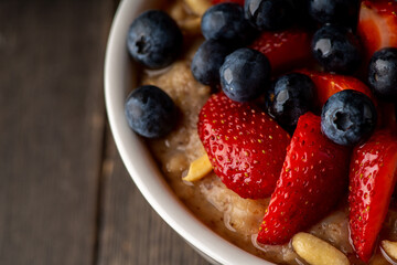 Oatmeal with ripe strawberries, blueberries and honey in the bowl. Selective focus.