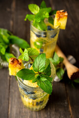 Refreshing mojito cocktail with pineapples and blueberry on the rustic background. Selective focus.
