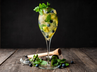 Refreshing mojito cocktail with pineapples and blueberry in wineglass on the rustic background. Selective focus.