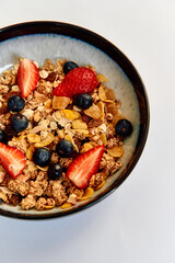 A delicious breakfast bowl filled with granola, fresh strawberries, blueberries, and crunchy cereal, offering a nutritious start to the day.