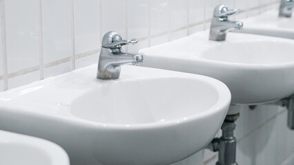 Public bathroom with white ceramic sinks and chrome faucets on clean wall