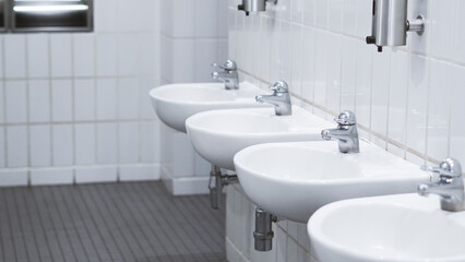 Public bathroom with white ceramic sinks and chrome faucets on clean wall
