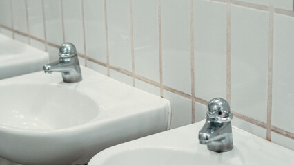 Public bathroom with white ceramic sinks and chrome faucets on clean wall