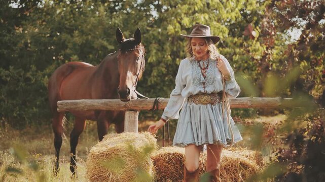 Happy Woman cowgirl with horse holds lasso rope walking in meadow forest tree leaves. bale of hay dry grass straw field nature summer ranch. leather hat sexy Girl boho dress country style wild west