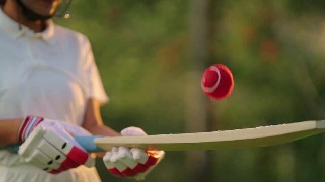 unknown athlete sports woman hand close up hold bat play with red ball outdoor ground. female girl cricket player wear white uniform protective helmet gloves standing at match playground