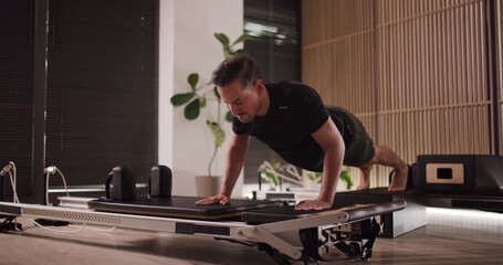 A man engages in a challenging workout on a reformer machine in a sleek fitness studio. He focuses intently as he executes push-ups, demonstrating strength and form - Powered by Adobe