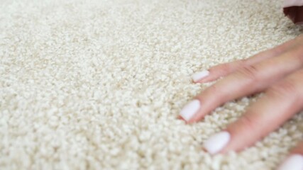 a woman's hand touching the beige Interior pile carpet made of polypropylene. 