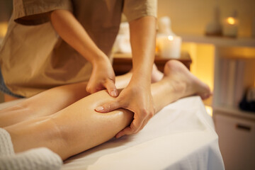 Close-up of therapist giving a relaxing leg massage in a calming spa setting with warm lighting. Health and wellness concept.