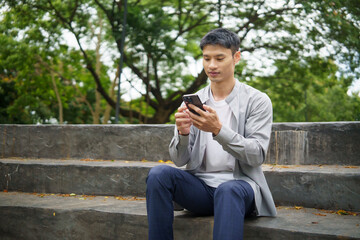 Obraz premium Adult asian man checking messages on mobile device during a break outside.