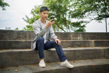 Obraz premium Relaxed male enjoying a pleasant moment browsing or texting on his phone in a sunny park.