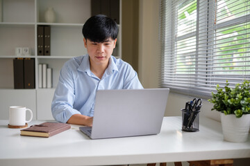 Fototapeta premium Young businessman focused on work while using a laptop in a modern office.