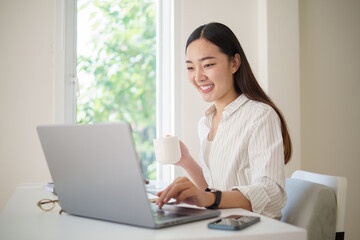 Focused businesswoman working on a laptop while enjoying a hot beverage in a bright modern office.