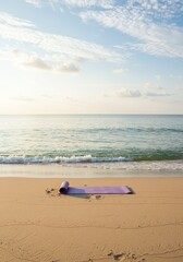 Fototapeta premium Purple yoga mat rolled on a sandy beach with ocean waves.
