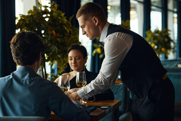 Caucasian young adult man serving wine to Caucasian young adult man and Caucasian young adult woman...