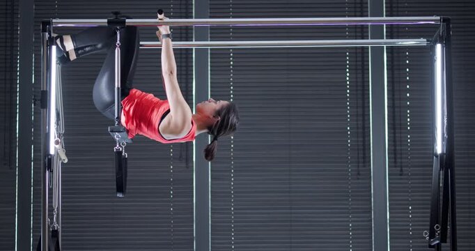 A skilled athlete performs a gravity-defying exercise, showcasing balance and strength while hanging upside down from gym equipment. The setting features bright lighting and a contemporary atmosphere