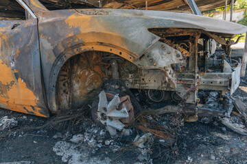 Fototapeta premium Burnt carcasses covered in ash and mud show twisted metal and melted structures. Destroyed car interior. Consequences of military conflict and shelling. Destroyed parking lot.